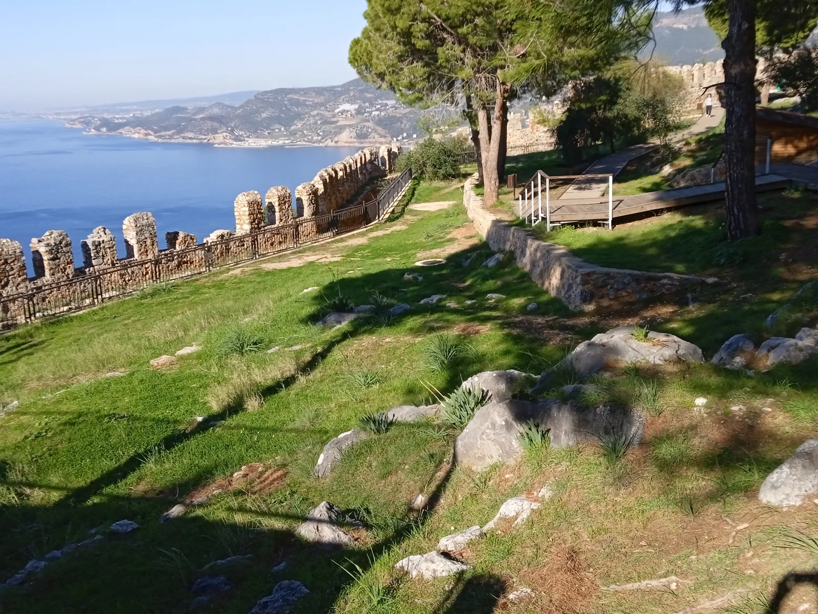 Burgberg von Alanya am 28. Dezember 2023, grüne Wiese und Pinien in der Sonne, dahinter das Meer